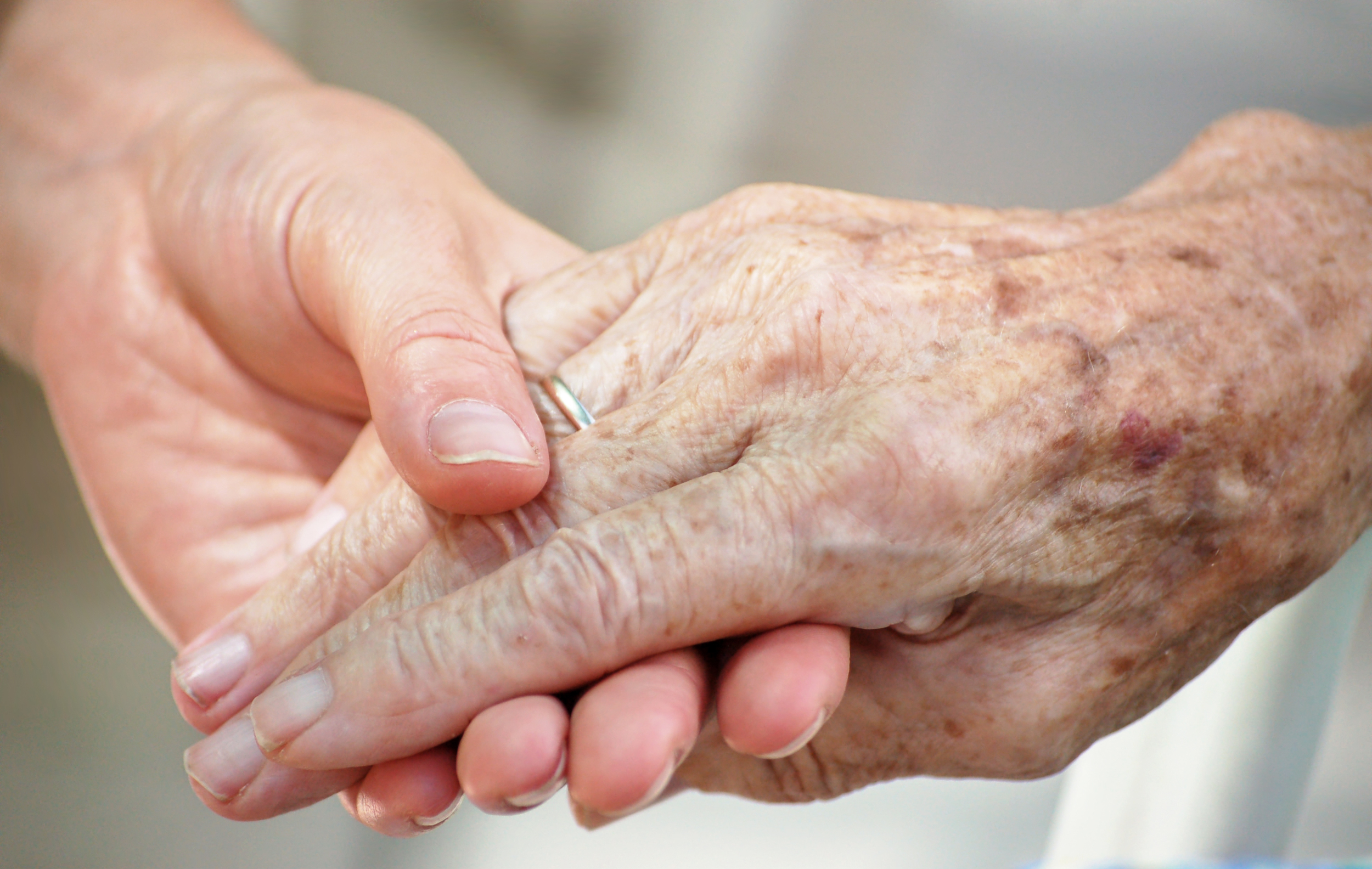 Two people holding hands gently, one with younger skin and the other with older, aged skin featuring prominent veins and age spots, symbolizing care or support.