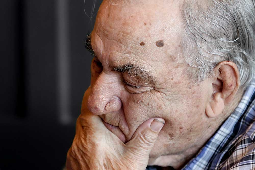 Caregiver offering comfort by placing their hand on the hands of a senior man who is holding a cane