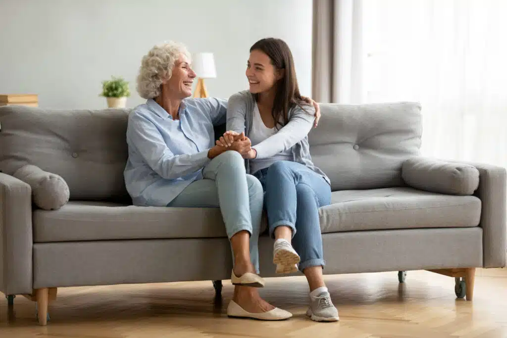 Happy senior woman sitting on couch at home holding hands with loved one