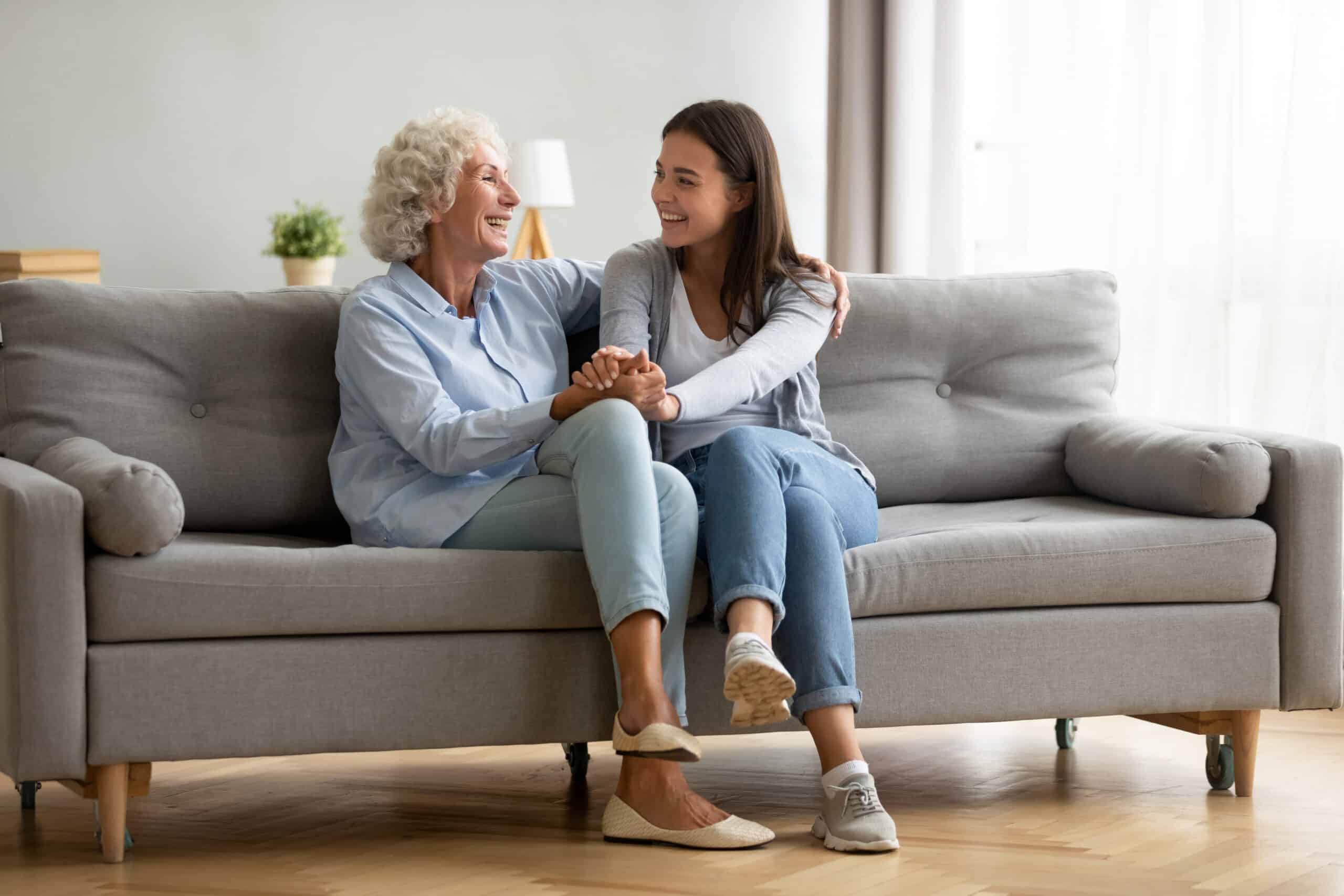 Happy senior woman sitting on couch at home holding hands with loved one
