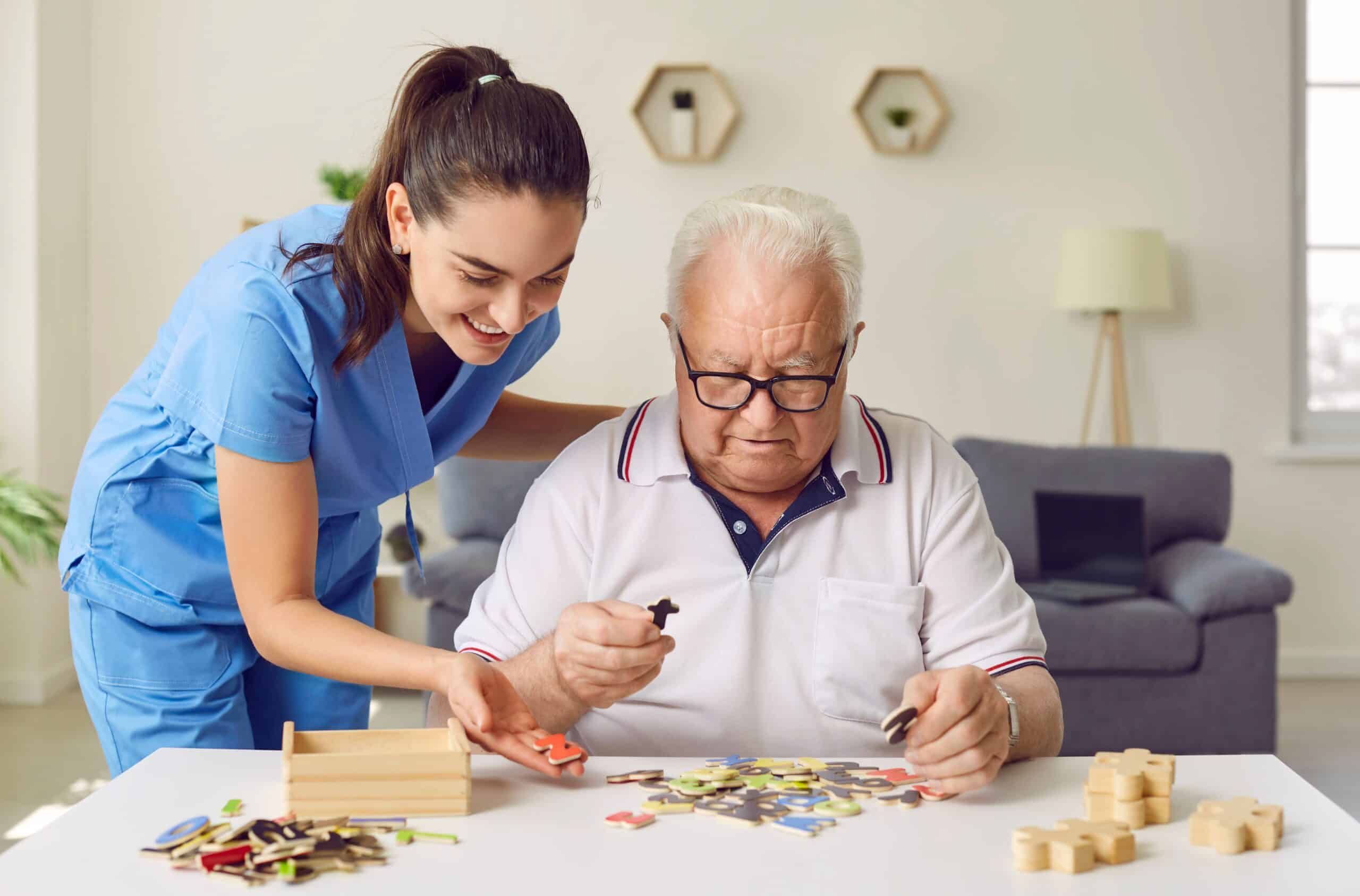 Older man sitting at a table with his live-in care attendant helping him complete a puzzle