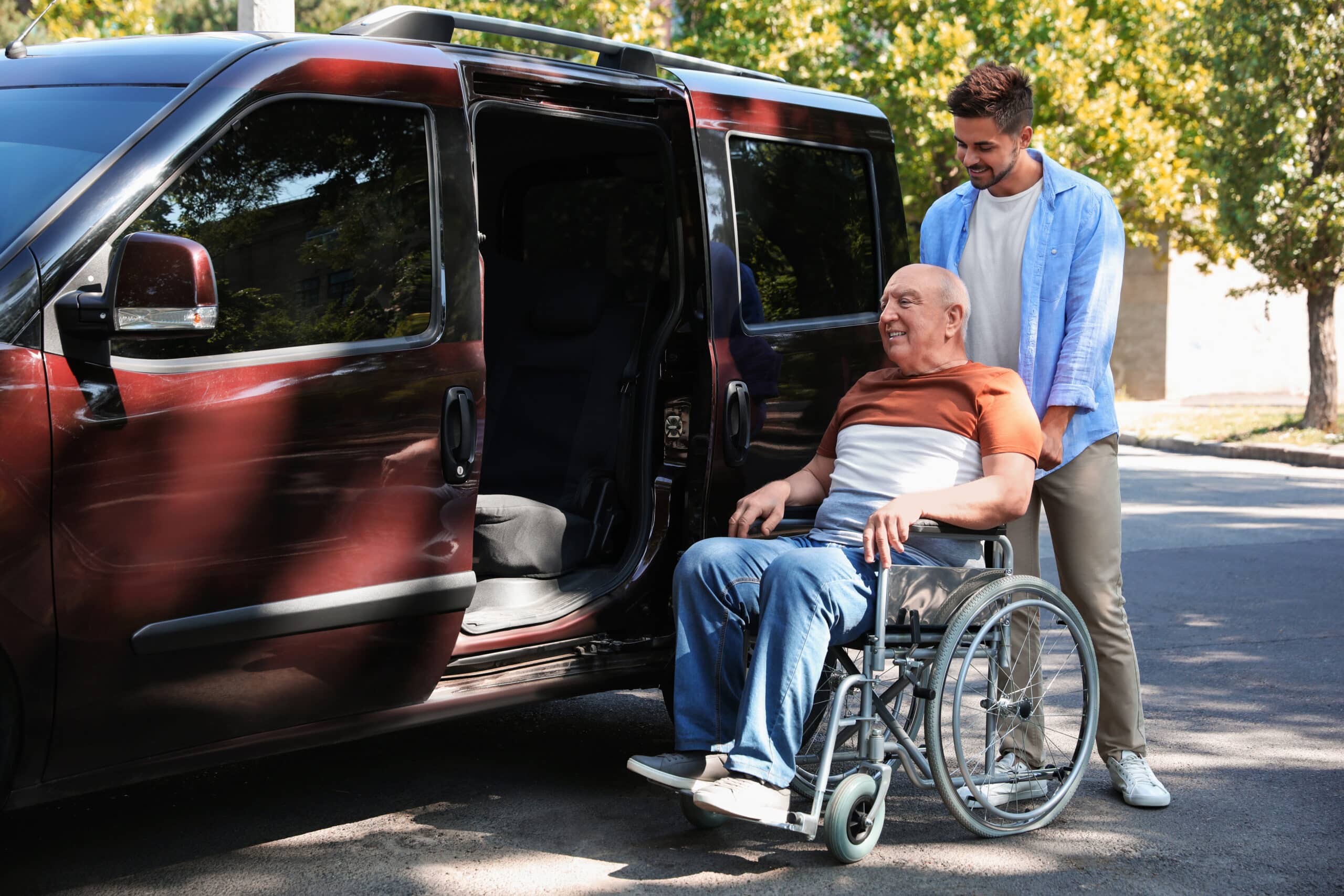 Older man in wheelchair being helped into vehicle by rideshare driver