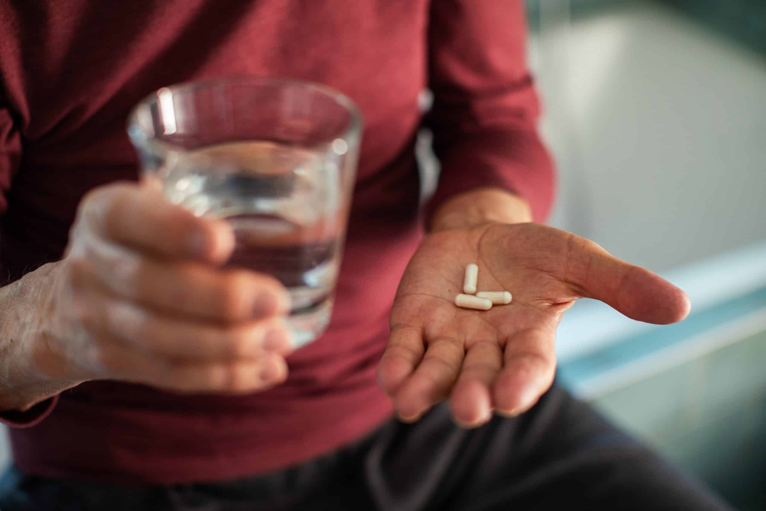 Old man with glass of water in one hand and medication in the other