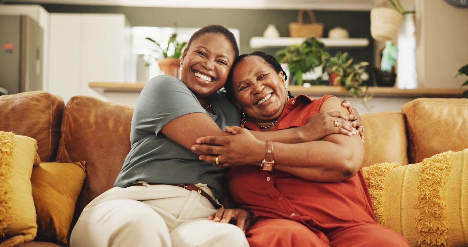 A mother and daughter smiling and hugging while sitting on a couch in a living room.