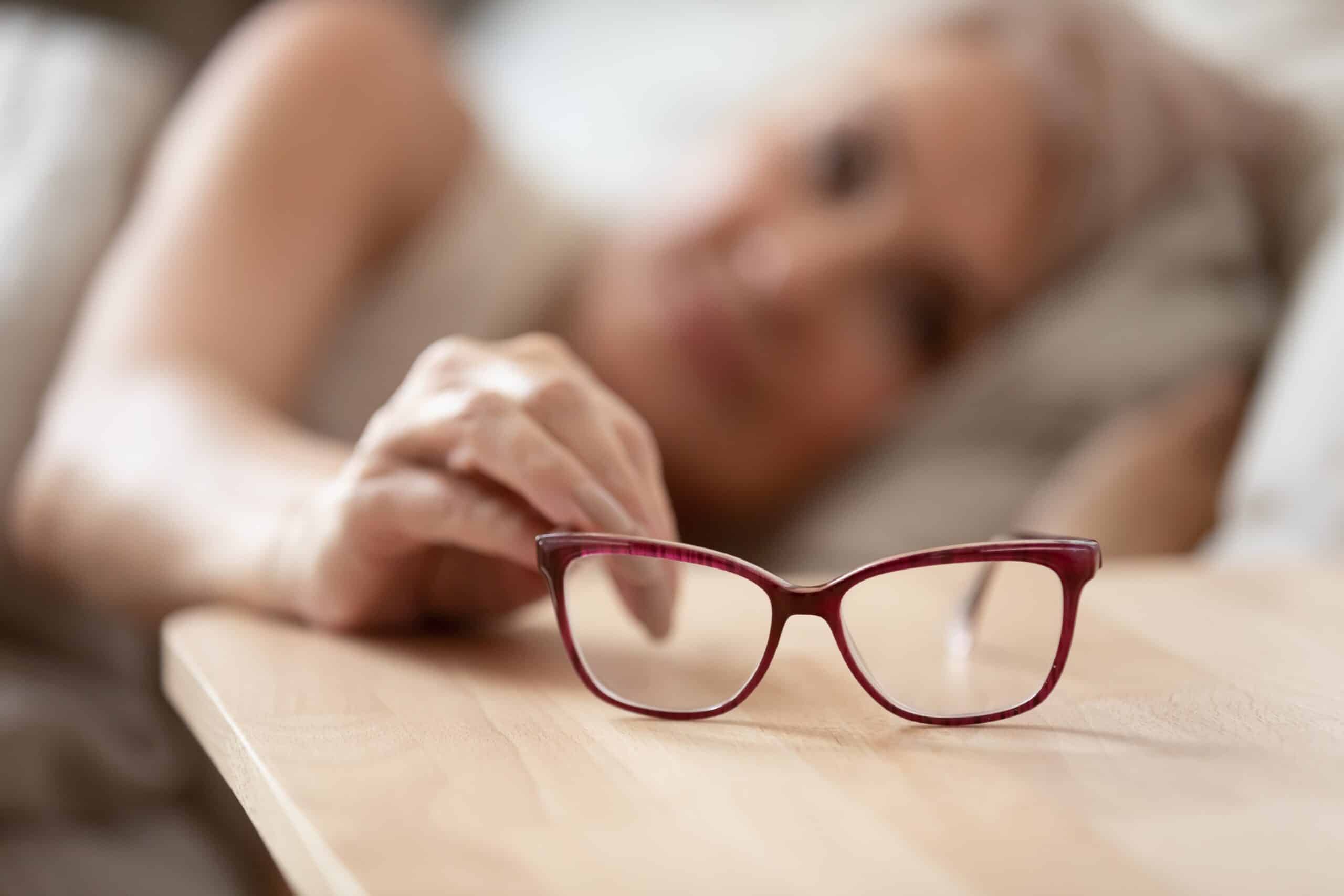 senior woman grabbing her glasses close from her bed