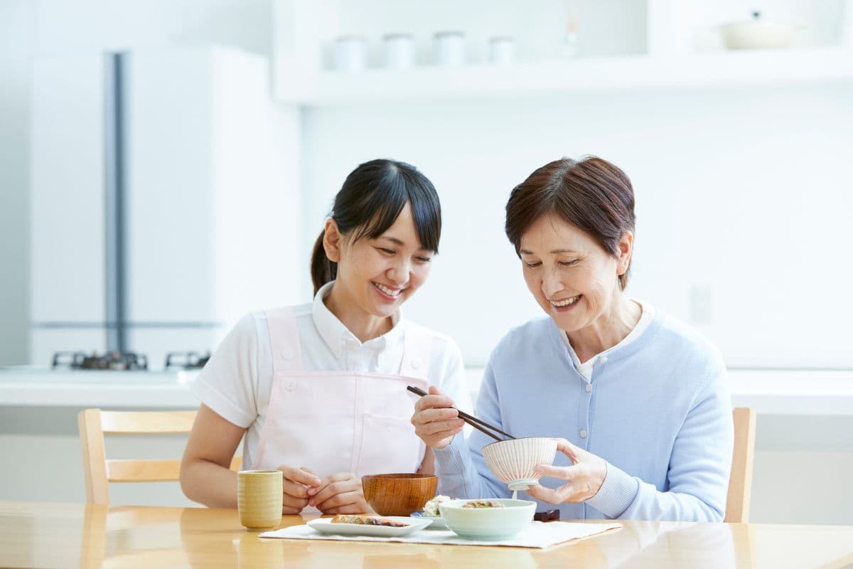 In-home caregiver with aging parent sharing a meal