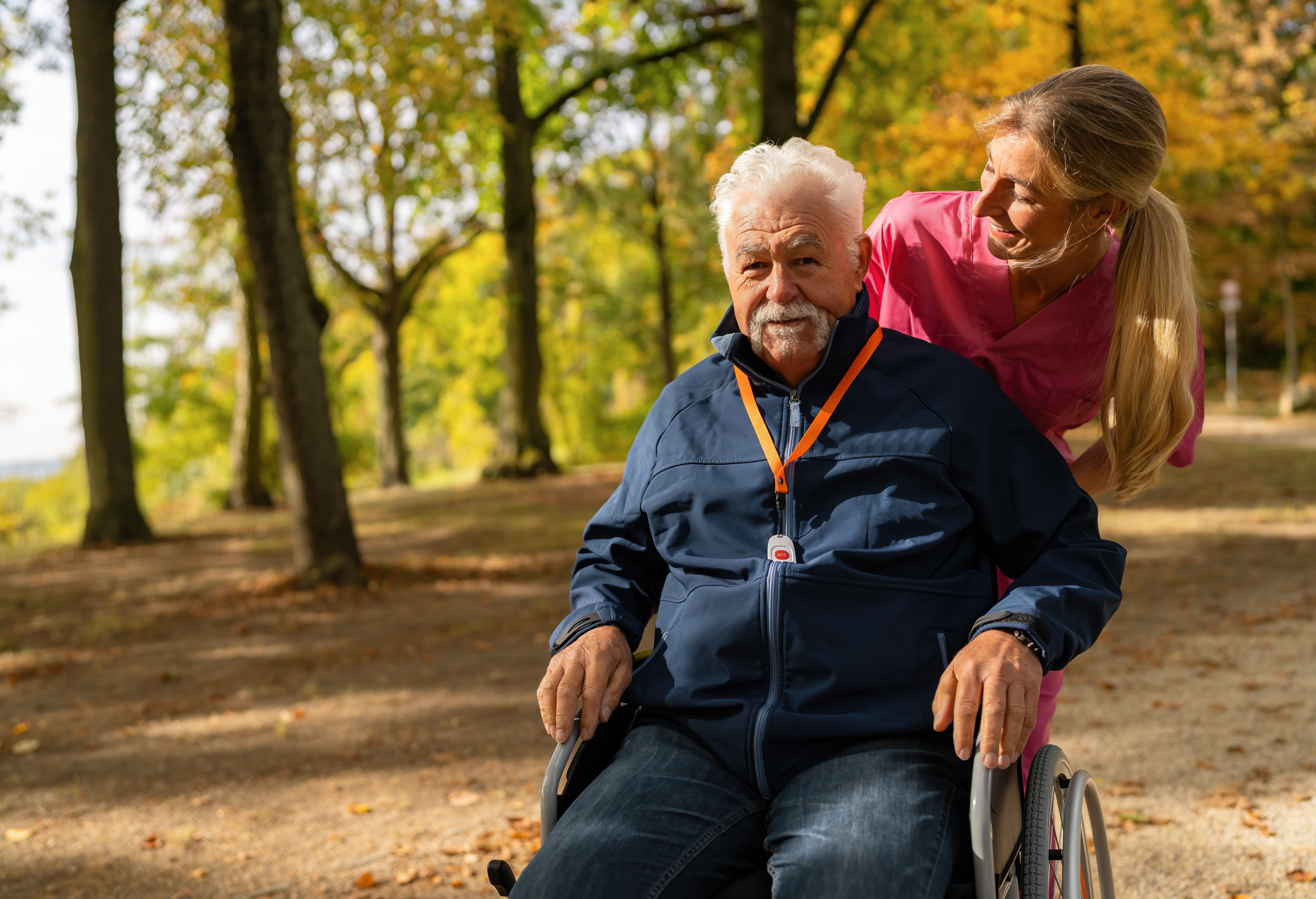 Caregiver caring for senior man in a wheechair while he's wearing a medical alert system
